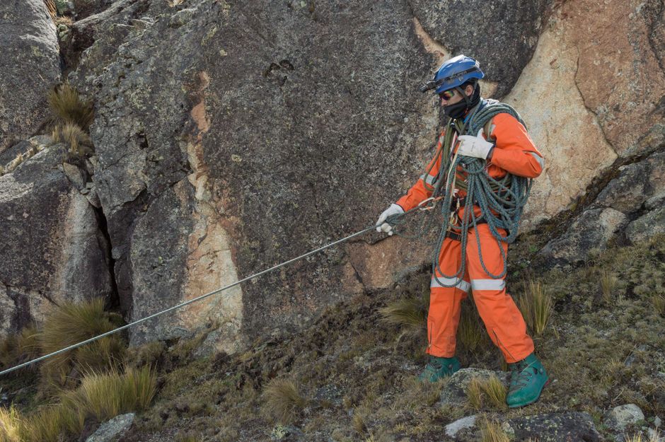 A rescuer in orange gear rappels down a rocky mountain slope, demonstrating expertise in rough terrain.