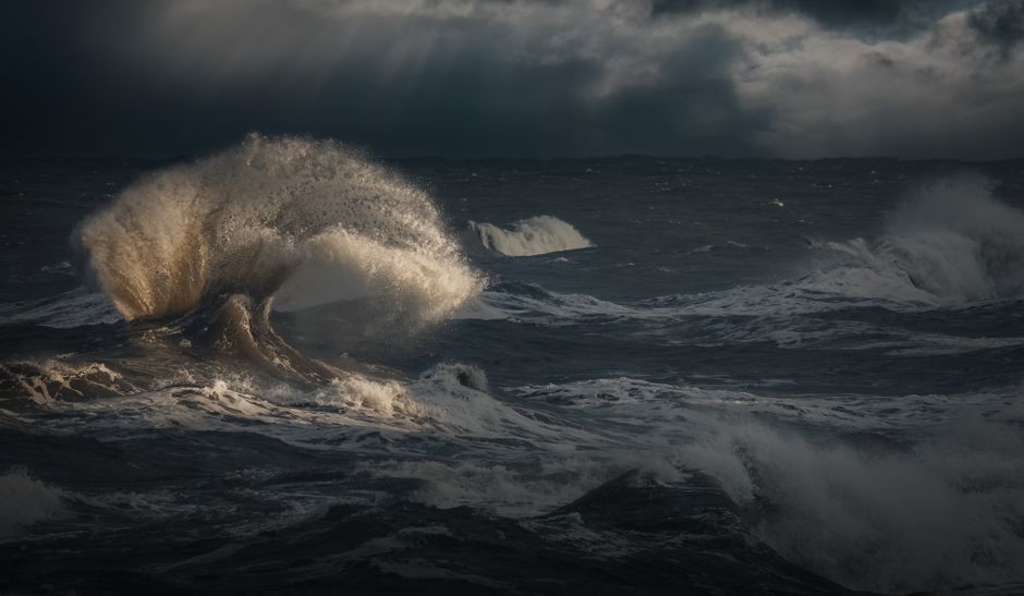 Powerful waves crash under dark stormy skies, capturing nature's raw energy and beauty.