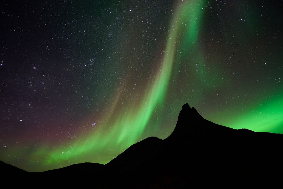 A mesmerizing display of northern lights dancing over a mountainous silhouette and starry night sky.