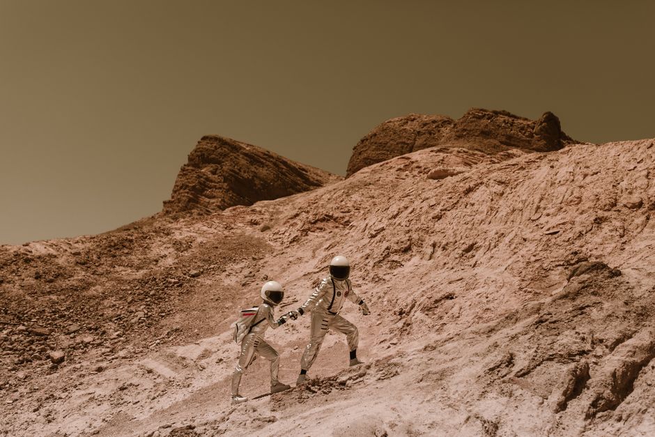 Two astronauts exploring a barren, alien landscape, resembling Mars.